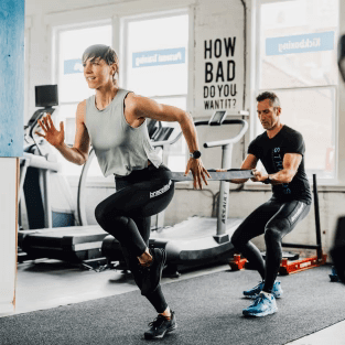 Two people in a gym, one person is running into a resistance band, the other is holding the resistance band behind her. getbracelayergoods.compression pants, compression tights, Exercises for knee strength, knee support, knees support, Vancouver knee brace, brace