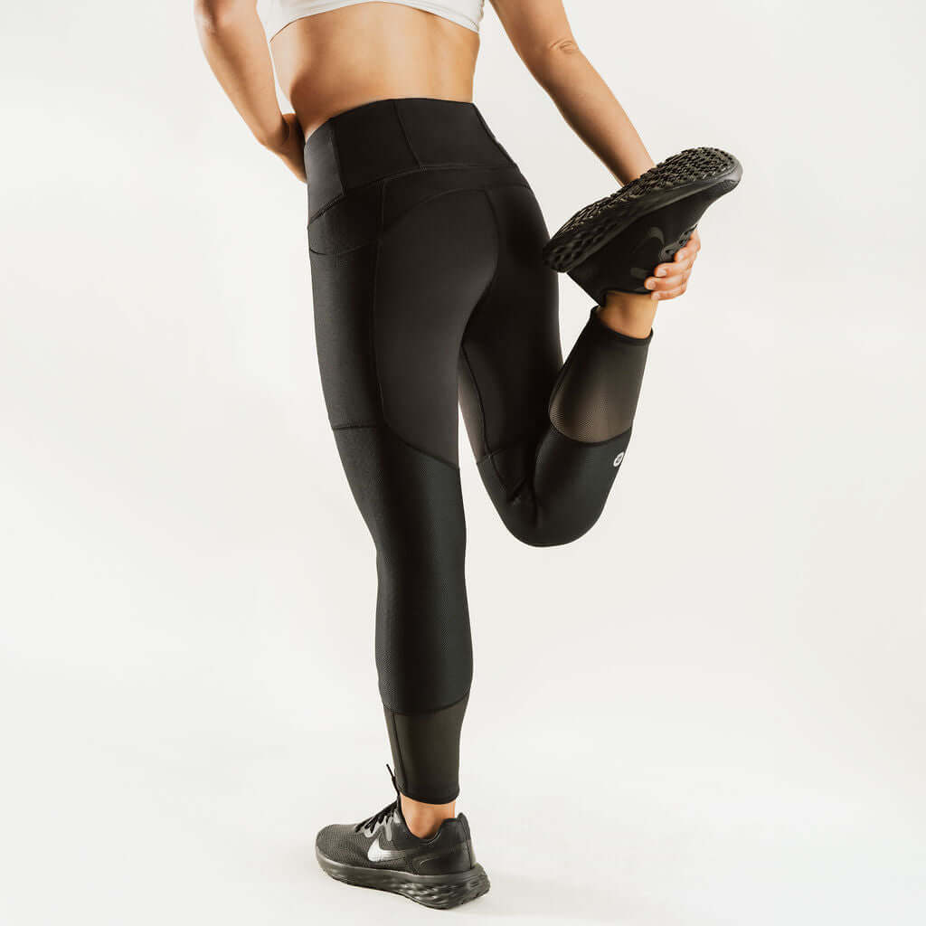 Black 7/8 knee support compression pants worn with sneakers, full leg view